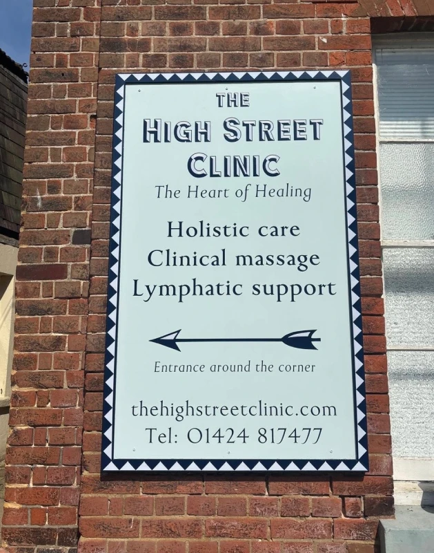The painted sign for The High Street Clinic on a brick wall: a pale board with navy lettering and an arrow reading 'Entrance around the corner'.
